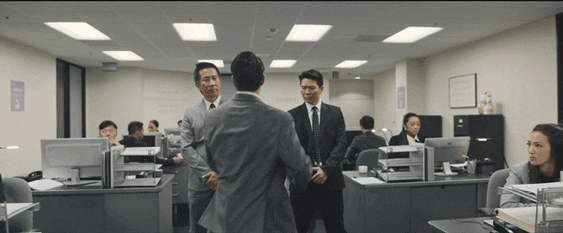 Hombre de traje bailando frente a sus compañeros en una oficina de ambiente serio y profesional. Sus movimientos son exagerados, mientras los demás lo observan con expresiones de sorpresa e incomodidad.