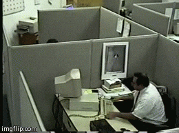 Hombre sentado en una oficina, visiblemente furioso, levanta el teclado y golpea con fuerza la pantalla de su computadora, haciéndola caer al piso. Su expresión y movimientos reflejan una explosión de ira.
